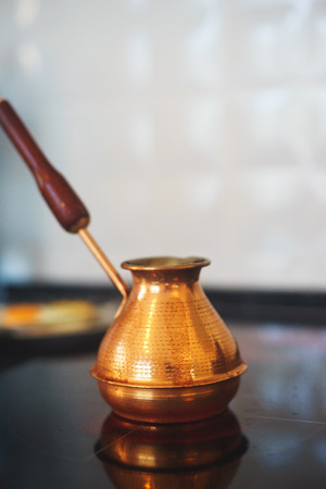 Classical copper turka for cooking coffee on a glass hob in a modern kitchen. Kitchenware. How to make coffee. Soft focus and beautiful bokeh.の写真素材