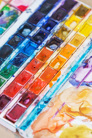 Abstract background concept for school watercolor. Hobbies and education, a cuvette with different watercolors. The artist's tools while working with paint. Stains of paint on special plastic containers. Brushes and watercolors.の写真素材