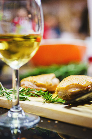 Glass of white wine and roasted turkey fillets on the table. Cooked turkey breast in orange sauce on a wooden board with rosemary and a glass of wine. Soft focus and beautiful bokeh.の写真素材