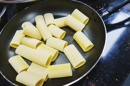 Classic penne with mussels and tomatoes in a frying pan. Process of cooking traditional pasta with seafood. Ingredients and stages of cooking in the kitchen. Penne close-up. Soft focus and bokeh.の写真素材
