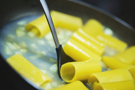 Classic penne with mussels and tomatoes in a frying pan. Process of cooking traditional pasta with seafood. Ingredients and stages of cooking in the kitchen. Penne close-up. Soft focus and bokeh.の写真素材