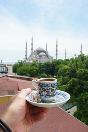 Man holds a traditional cup of coffee in his hand with a Blue mosque Sultanahmet Camii background.Travel to Istanbul, Turkey. Soft focus and beautiful bokeh.の写真素材