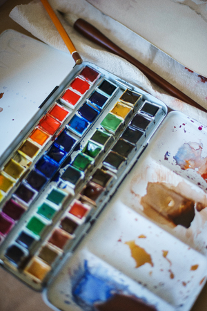 Spots of watercolor paint on a cuvette with different watercolors. Drawing and art. Abstract background. Soft focus and beautiful bokeh. Stains of paint on special plastic containers.の写真素材