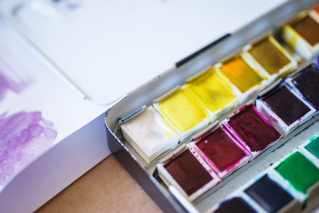 Spots of watercolor paint on a cuvette with different watercolors. Drawing and art. Abstract background. Soft focus and beautiful bokeh. Stains of paint on special plastic containers.の写真素材