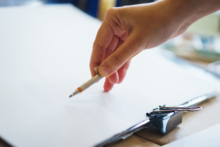 Artist with a pencil close-up while drawing a sketch on clean paper. Preparation and drawing for watercolor painting.の写真素材