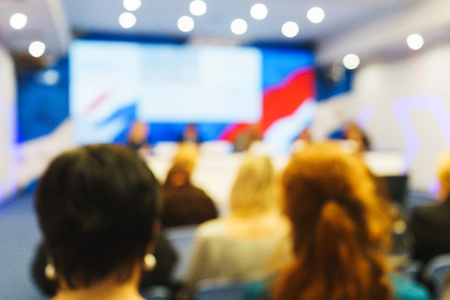 People listen to the speaker in the audience during a press conference, event, lecture or presentation from behind. Blurred image of participants of the conference in the lecture hall. Reportage.の写真素材