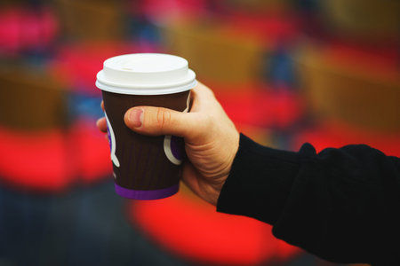 Brown paper cup in hand. Student, office worker holding a plastic paper cup in the audience. A young...