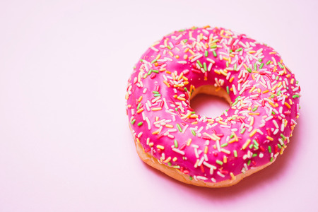 Bright donut in a pink glaze with a multi-colored rainbow sprinkle on a pink background. Sweets and desserts. Minimalistic background with clean place for the inscription. Copy space. Soft focus.の写真素材