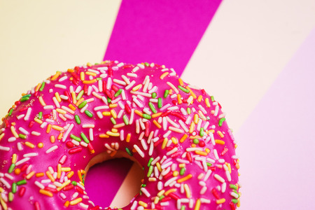 Bright pink sweet donut with pink icing and multi-colored powder on a multicolored background. Sweet and desserts for the holiday. Bakery products. Soft focus and beautiful bokeh. Colorful doughnut.の写真素材