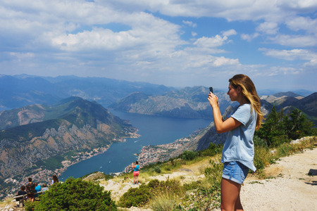 Traveler smartphone, landscape photography. Attractive girl takes story on smartphone while traveling mountains in Montenegro. Magical view Boko-Kotorska bay. Famous place in Montenegro. Kotor.の写真素材