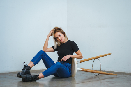 Model tests. Photo session model in studio. Simple attractive portraits for a young beautiful girl in an empty room. Snaps. Attractive girl in jeans,  black shirt. Cheerful girl sitting on the floorの写真素材