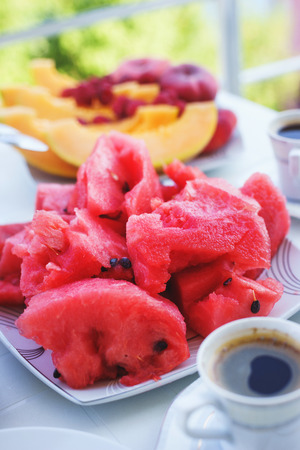 Traditional breakfast is fragrant black coffee with fresh fruits, watermelon and melon on the table. Healthy diet and vegetarian diet. Journey. Summer holidays by the seaの写真素材