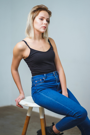 Model tests. Photo session model in studio. Simple attractive portraits for a young beautiful girl in an empty room. Snaps. Attractive girl in jeans,  black shirt. Cheerful girlの写真素材