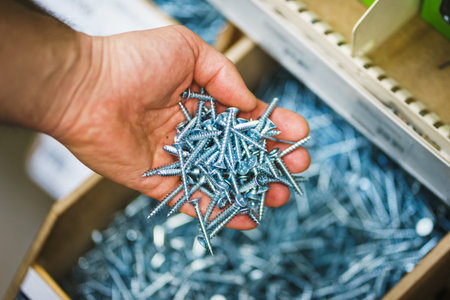 Man holds in his hands many silver small screws for repair and fasteners in a box close-up.