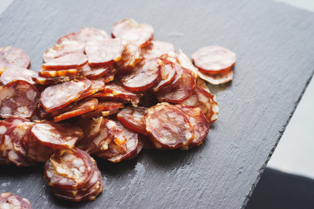 Thinly sliced sausage slices on a black stone board. Traditional meat products, boiled and smoked sausage. Ingredients for cooking. Abstract food background. Soft focus.の写真素材