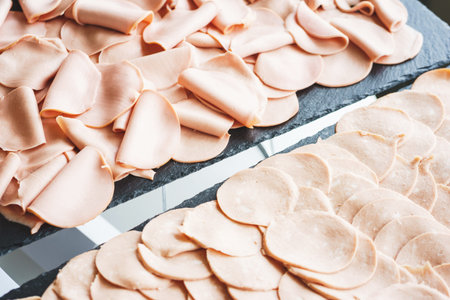 Thinly sliced sausage slices on a black stone board. Traditional meat products, boiled and smoked...