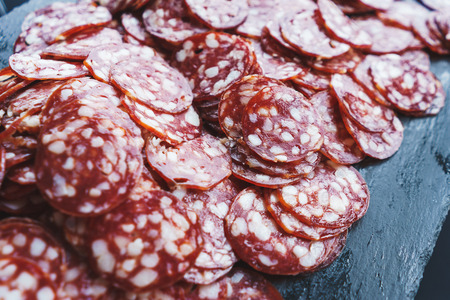 Thinly sliced sausage slices on a black stone board. Traditional meat products, boiled and smoked sausage. Ingredients for cooking. Abstract food background. Soft focus.の写真素材