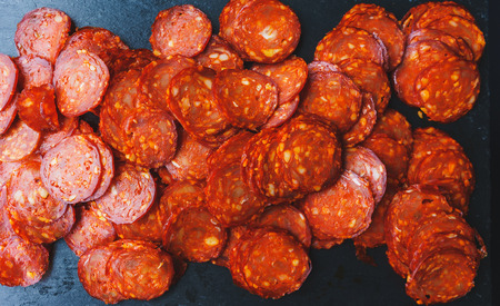 Thinly sliced sausage slices on a black stone board. Traditional meat products, boiled and smoked sausage. Ingredients for cooking. Abstract food background. Soft focus.の写真素材