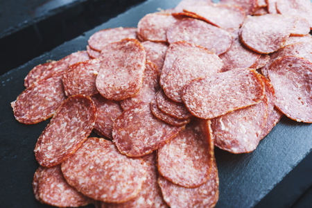 Thinly sliced sausage slices on a black stone board. Traditional meat products, boiled and smoked sausage. Ingredients for cooking. Abstract food background. Soft focus.の写真素材