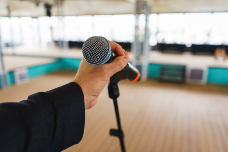 Man holds a hand microphone during a rehearsal on the stage. Speech singer, speaker, during the event. Equipment and tools for performance. Man's hand with a microphone. Repetition.の写真素材