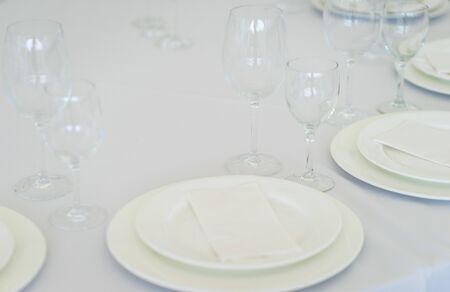 Clean empty glasses and plates on the table in the restaurant prepared for guests. Serving. White dishes and glasses for drinks. Soft focus and beautiful bokeh.の写真素材