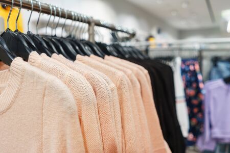 Modern fashion store. Buyers choose clothes. Shirts, hoodies, blouses and half-sweaters, a sweater on a hanger in a clothing store close-up. Sale and shopping in stores. Soft focus.の写真素材