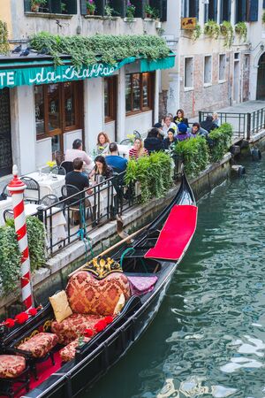 VENICE, ITALY - OCTOBER, 2019. Travelers in cute street restaurants and cafes on the canal embankment. Trip to Italy. Bright sunny autumn day. Canal in Venice. Beautiful gondola and promenade.のeditorial素材