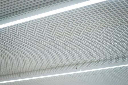 Lighting and ceiling finishes in of the modern ceilings and interior in the office. Lighting devices. Silver metal grill on the ceiling.の写真素材