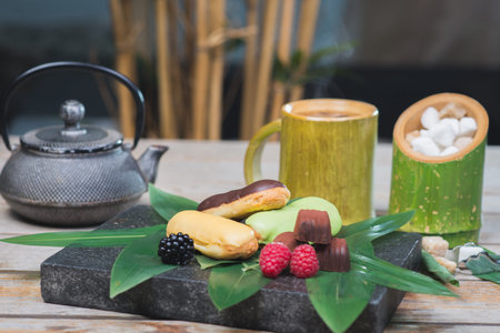 Sweet dessert, eclairs, raspberries and chocolate candies on a wooden table with decor in oriental,...