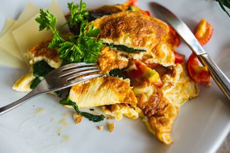 Traditional omelet with vegetables, spinach, tomatoes and herbs on a wooden table in a restaurant. Classic european breakfast. Fried eggs with milk and cheese. Soft focus.の写真素材