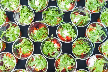 Mini appetizer salad in a glass of tomatoes with mozzarella, arugula and pesto. Italian traditional food for guests and participants at the event. Catering and guest services.の写真素材