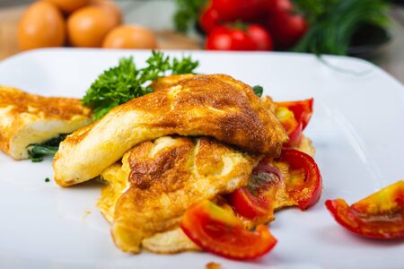 Traditional omelet with vegetables, spinach, tomatoes and herbs on a wooden table in a restaurant. Classic european breakfast. Fried eggs with milk and cheese. Soft focus.の写真素材