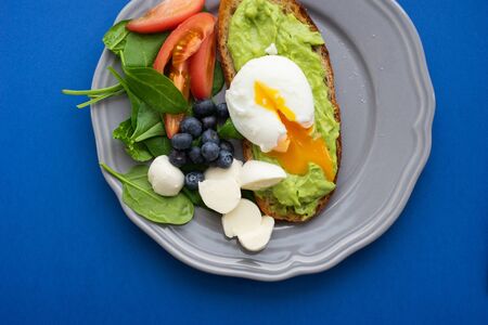 Wholesome tasty full of vitamins and health breakfast with avocado, berries, cheese and tomatoes with basil on classic blue background. Detox. Healthy food. Soft focus and beautiful bokeh.の写真素材