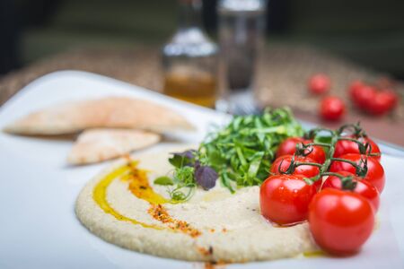 Traditional appetizer hummus with bread cakes, pita, on a plate with vegetables and sauce. Creative serving of classic snacks on a wooden table in a restaurant or cafe. Soft focus.の写真素材