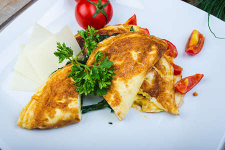 Traditional omelet with vegetables, spinach, tomatoes and herbs on a wooden table in a restaurant.の写真素材