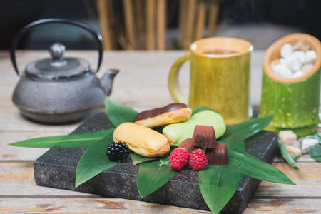 Sweet dessert, eclairs, raspberries and chocolate candies on a wooden table with decor in oriental, asian style.の写真素材