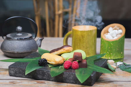 Sweet dessert, eclairs, raspberries and chocolate candies on a wooden table with decor in oriental, asian style.の写真素材