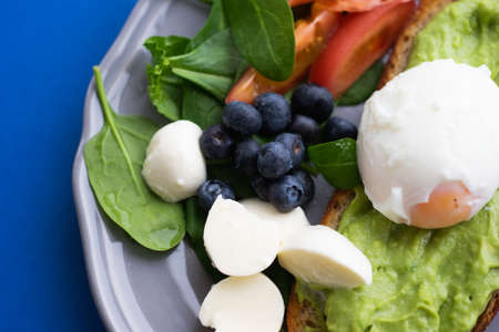 Wholesome tasty full of vitamins and health breakfast with avocado, berries, cheese and tomatoes with basil.の写真素材
