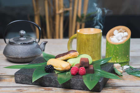 Sweet dessert, eclairs, raspberries and chocolate candies on a wooden table with decor in oriental, asian style.の写真素材