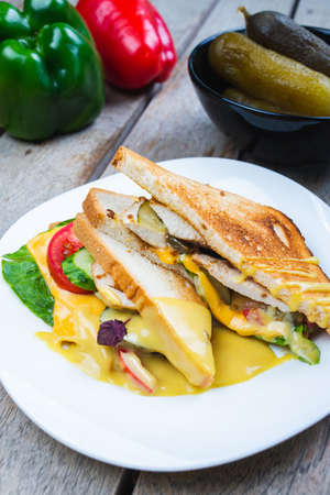Classic breakfast, hot sandwiches with cheese, vegetables and chicken on a wooden table.の写真素材