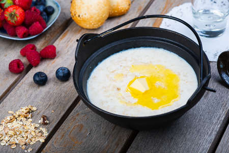 Traditional breakfast milk porridge with butter and berries on a wooden table.の写真素材