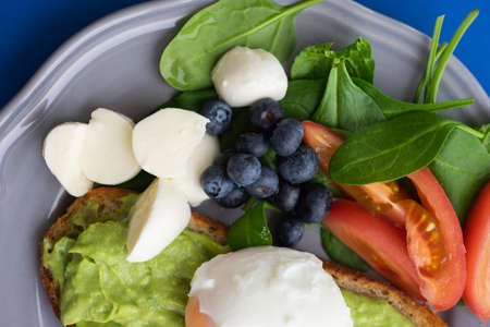 Wholesome tasty full of vitamins and health breakfast with avocado, berries, cheese and tomatoes with basil.の写真素材