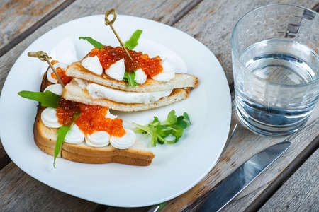 Classic breakfast, hot sandwich with red salmon caviar and mozzarella on a plate on a wooden table.の写真素材