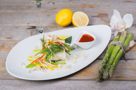 White fish seabass fillet with vegetables and white wine on a wooden table in a restaurant with decor.の写真素材