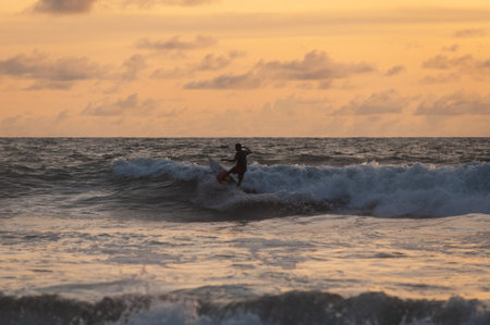 Surfing at sunset. Young people ride on short boards, perform tricks on the waves. Extreme sports and hobbies. Ocean waves. Soft focus and blurry photos while moving. Stylization and tinting. Concept.の写真素材