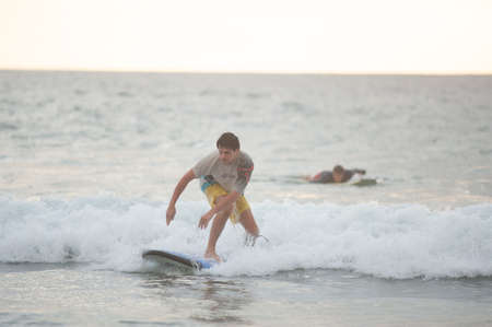 BALI, INDONESIA-MARCH 2020: Beginner surfer learns to row and ride on a training board in small waves in the ocean. Golden hour, sunset on the ocean. Extreme sport. Training. Concept.のeditorial素材