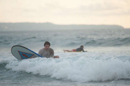 BALI, INDONESIA-MARCH 2020: Beginner surfer learns to row and ride on a training board in small waves in the ocean. Golden hour, sunset on the ocean. Extreme sport. Training. Concept.のeditorial素材