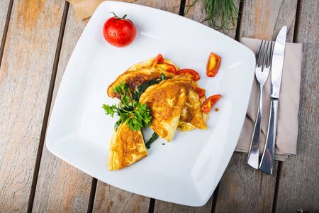 Traditional omelet with vegetables, spinach, tomatoes and herbs on a wooden table in a restaurant. Classic european breakfast. Fried eggs with milk and cheese. Soft focus.の写真素材