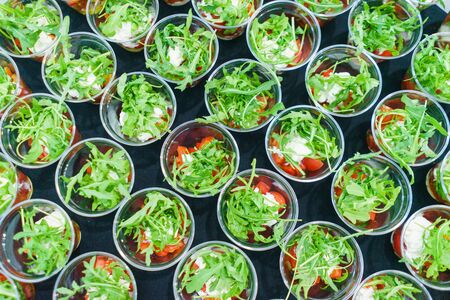 Mini appetizer salad in a glass of tomatoes with mozzarella, arugula and pesto. Italian traditional food for guests and participants at the event. Catering and guest services.の写真素材