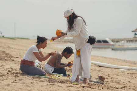 BALI, INDONESIA-APRIL, 2020: Traditional Balinese blessing ceremony by ocean, featuring newlyweds and an elder, shaman, monk or clergyman. Priest conduct the ceremony on the shore. Soft focus.のeditorial素材